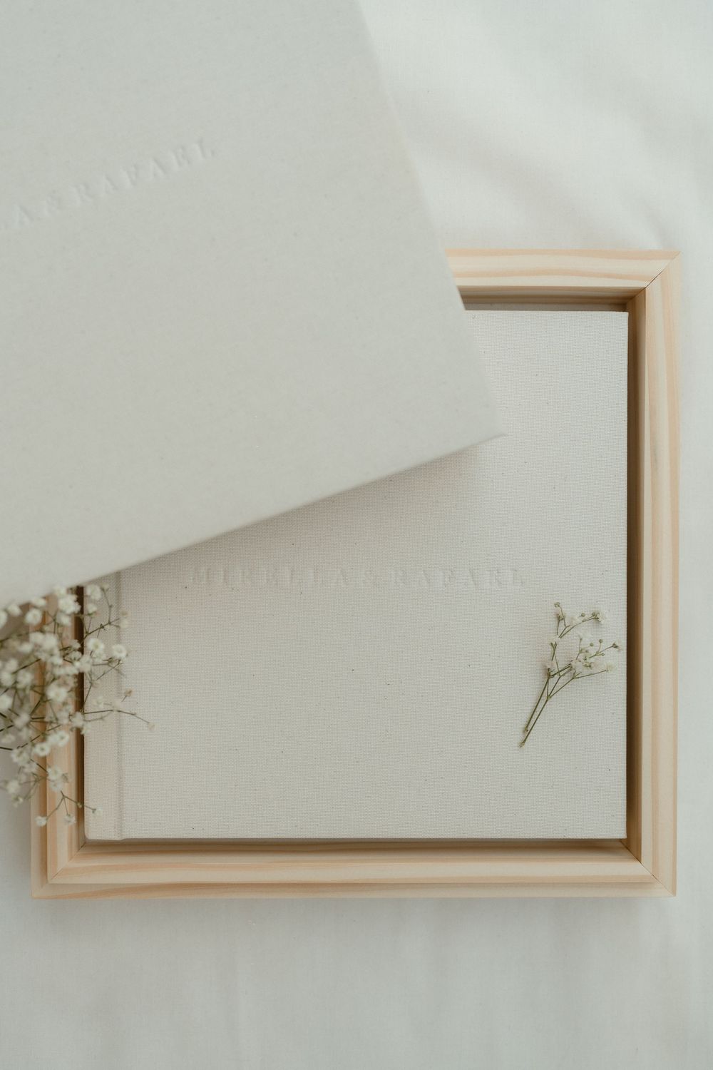Elegant white wedding album or photo book with delicate dried flowers in a minimalist wooden box frame.