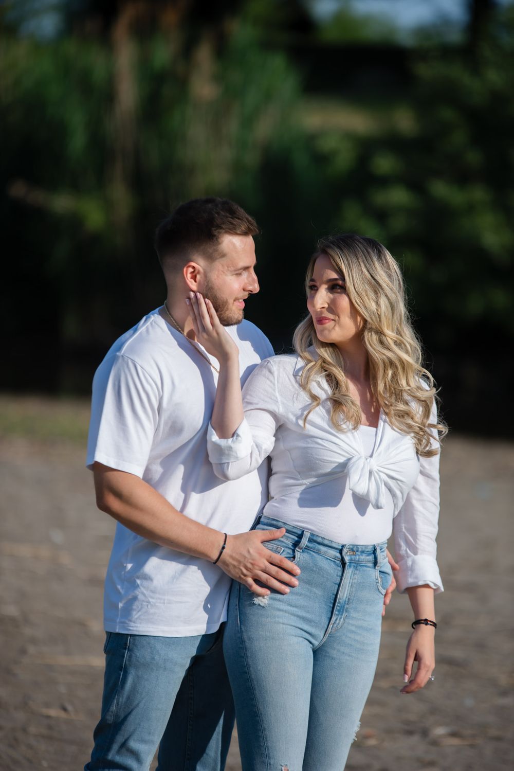 Young couple in matching white tops and jeans sharing a tender moment outdoors.