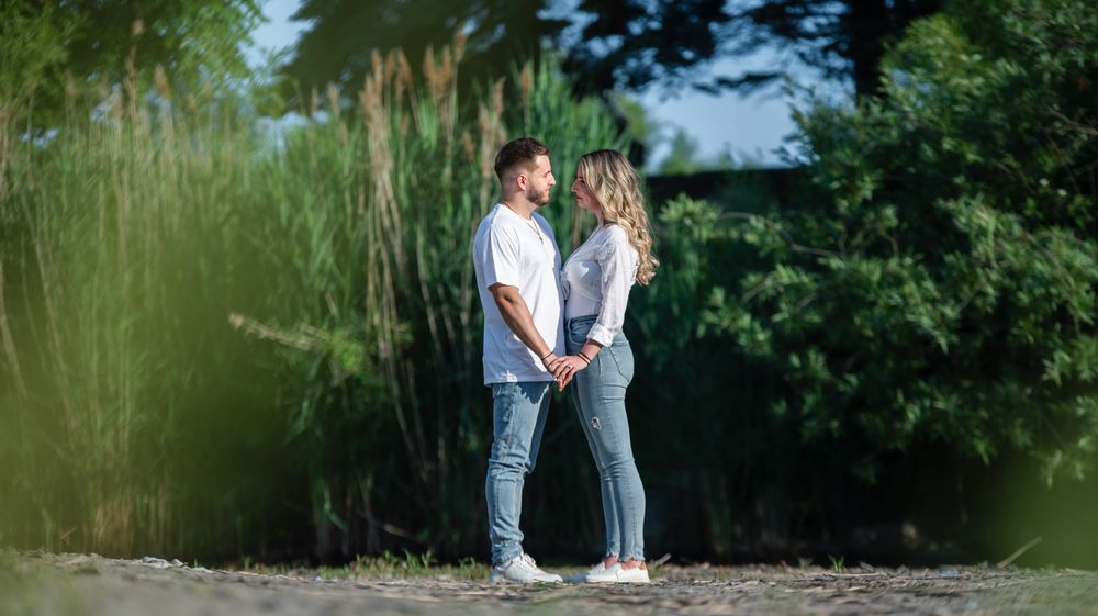 Couple facing each other holding hands on a sandy path with tall green reeds.