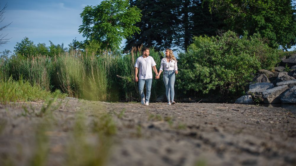 Couple walking hand in hand on a sandy path surrounded by lush green vegetation.