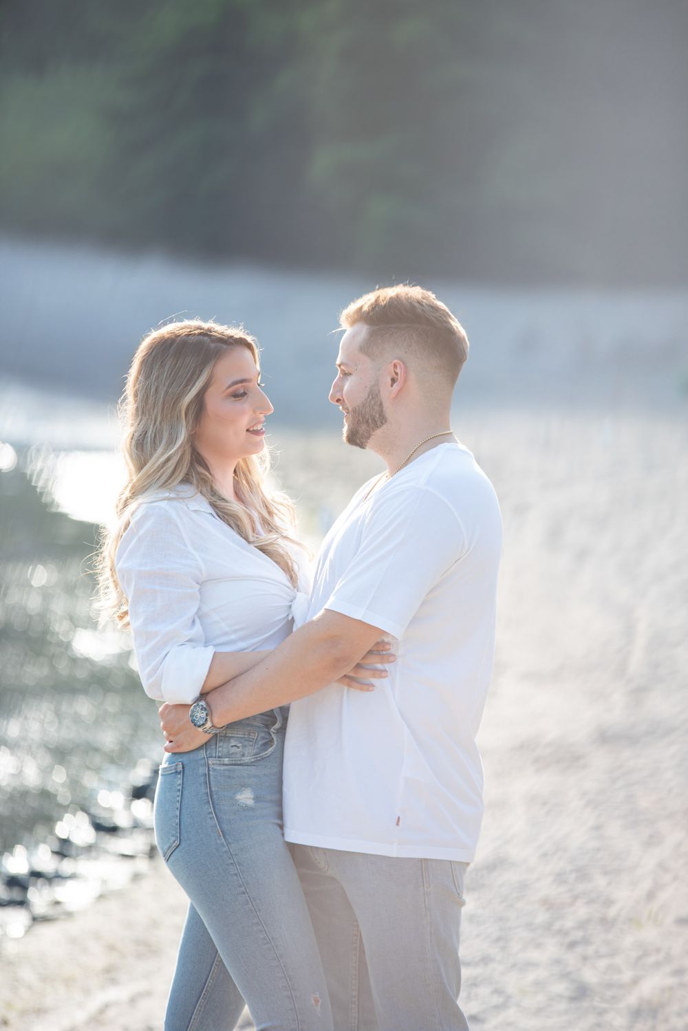 Romantic couple embracing and gazing into each others eyes on a bright sunlit sandy beach.