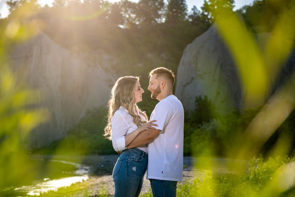 Romantic couple gazing into each others eyes in a sun-drenched natural landscape with rocky cliffs.