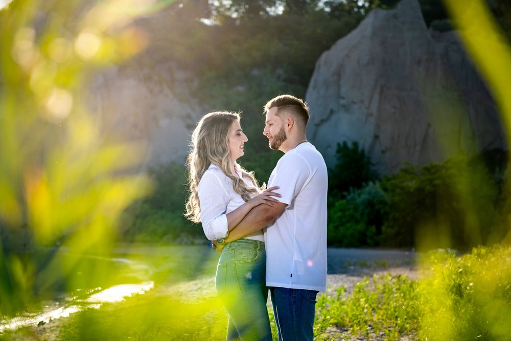 Romantic couple holding each other close near rocky landscape with golden sunlight behind them.