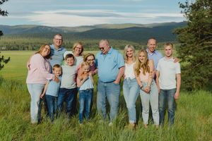Large family group portrait outdoors in a green meadow with mountain views in the background.