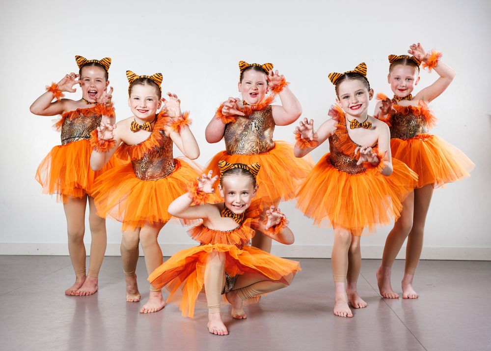 Six young girls in orange tiger costumes with tutus and ears posing for dance recital photo.