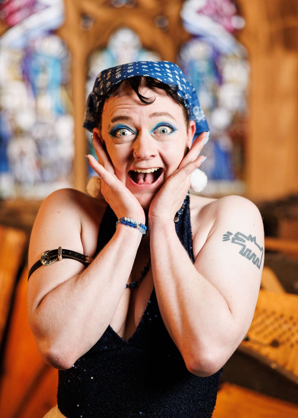 Person with blue headband and sparkly top makes exaggerated surprised expression in ornate church setting.