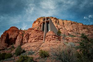 Chapel of the Holy Cross built into red rock formations in Sedona, Arizona under dramatic cloudy skies.