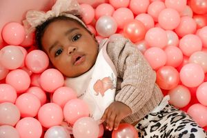 Adorable baby girl in pink ball pit wearing leopard print pants and bow headband.