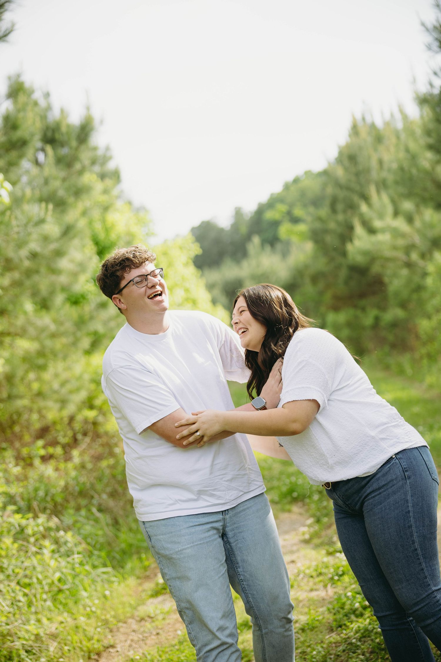 Laughing couple in matching white shirts and jeans sharing a joyful moment on a forest path.