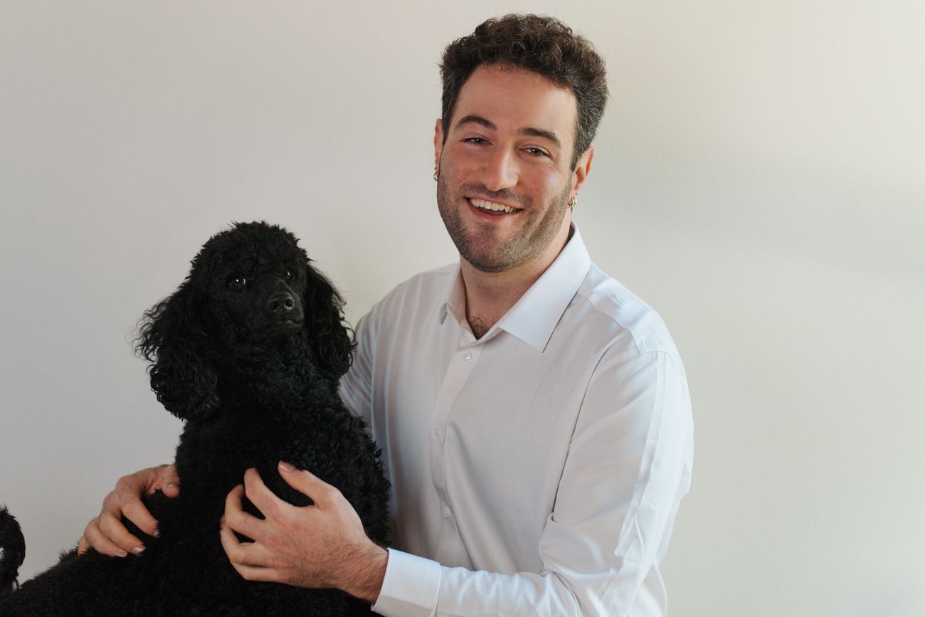 Smiling young man in white shirt posing with a black standard poodle dog against a white background dog photoshoot in Gables Sydney