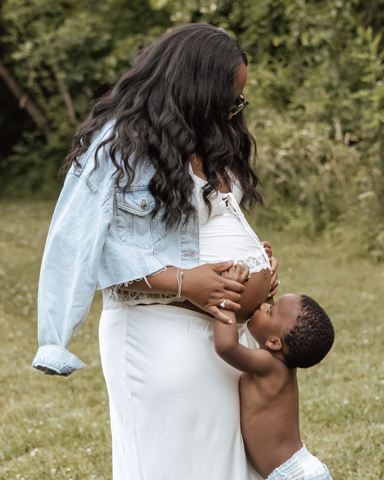 Pregnant woman in beige halter maxi dress cradling baby bump on sandy beach at golden hour.