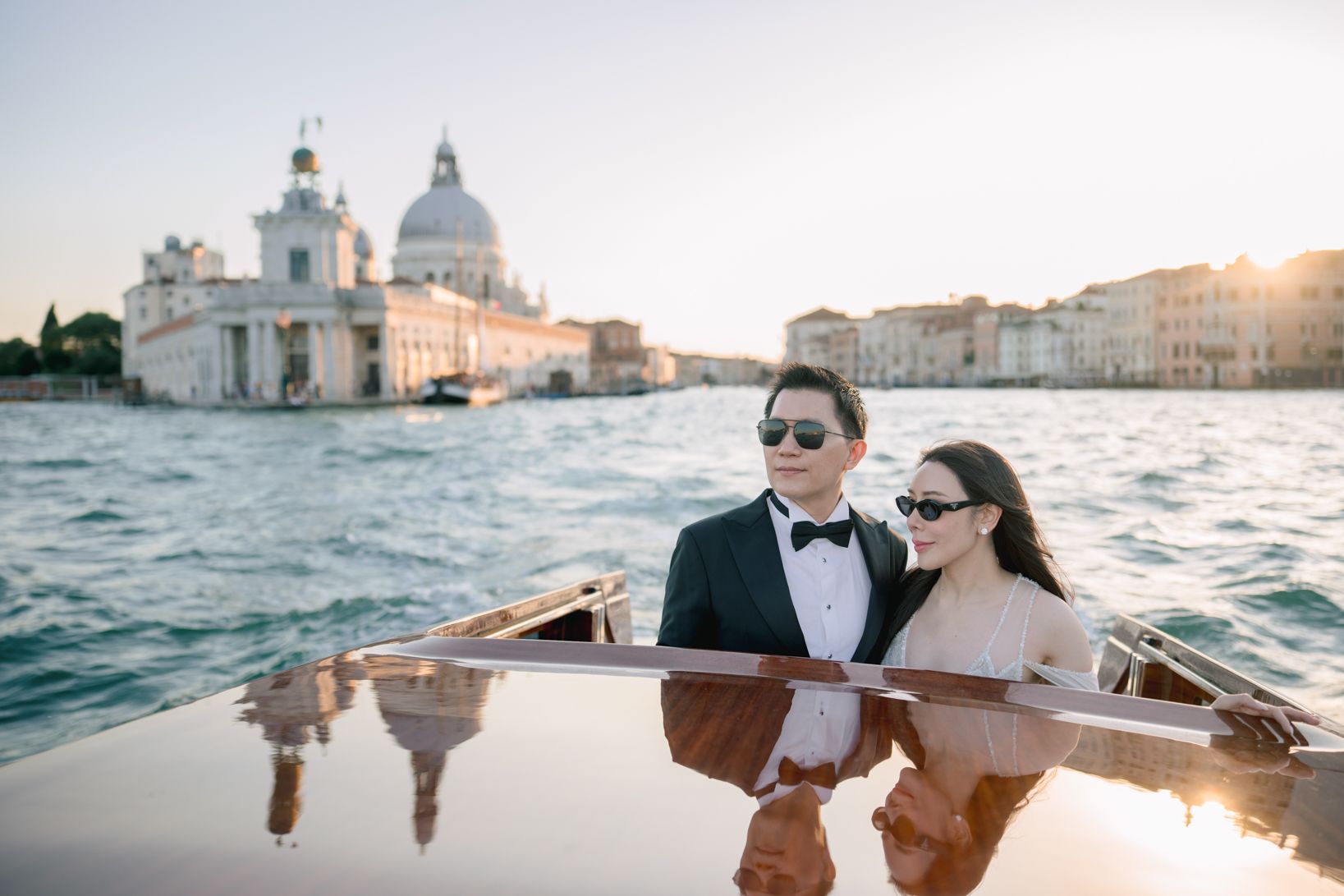 Couple in formal attire on a luxury boat in Venice with the Santa Maria della Salute basilica at sunset.
