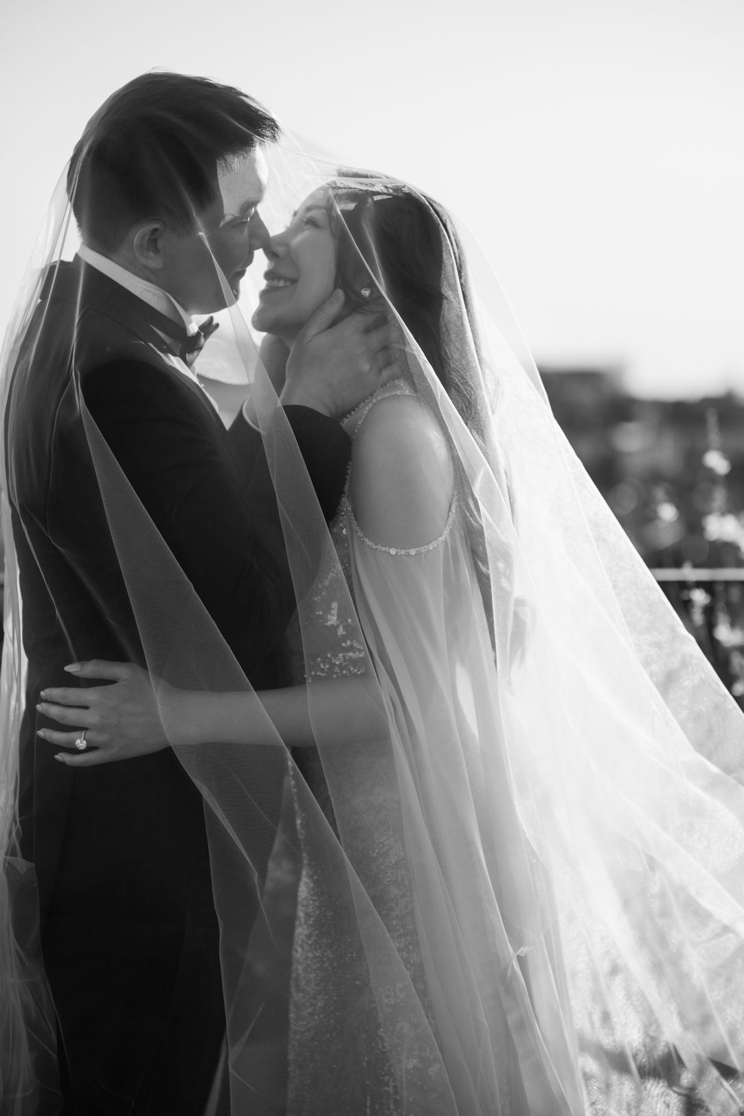 Black and white photo of a bride and groom sharing a romantic moment under her flowing veil on their wedding day.