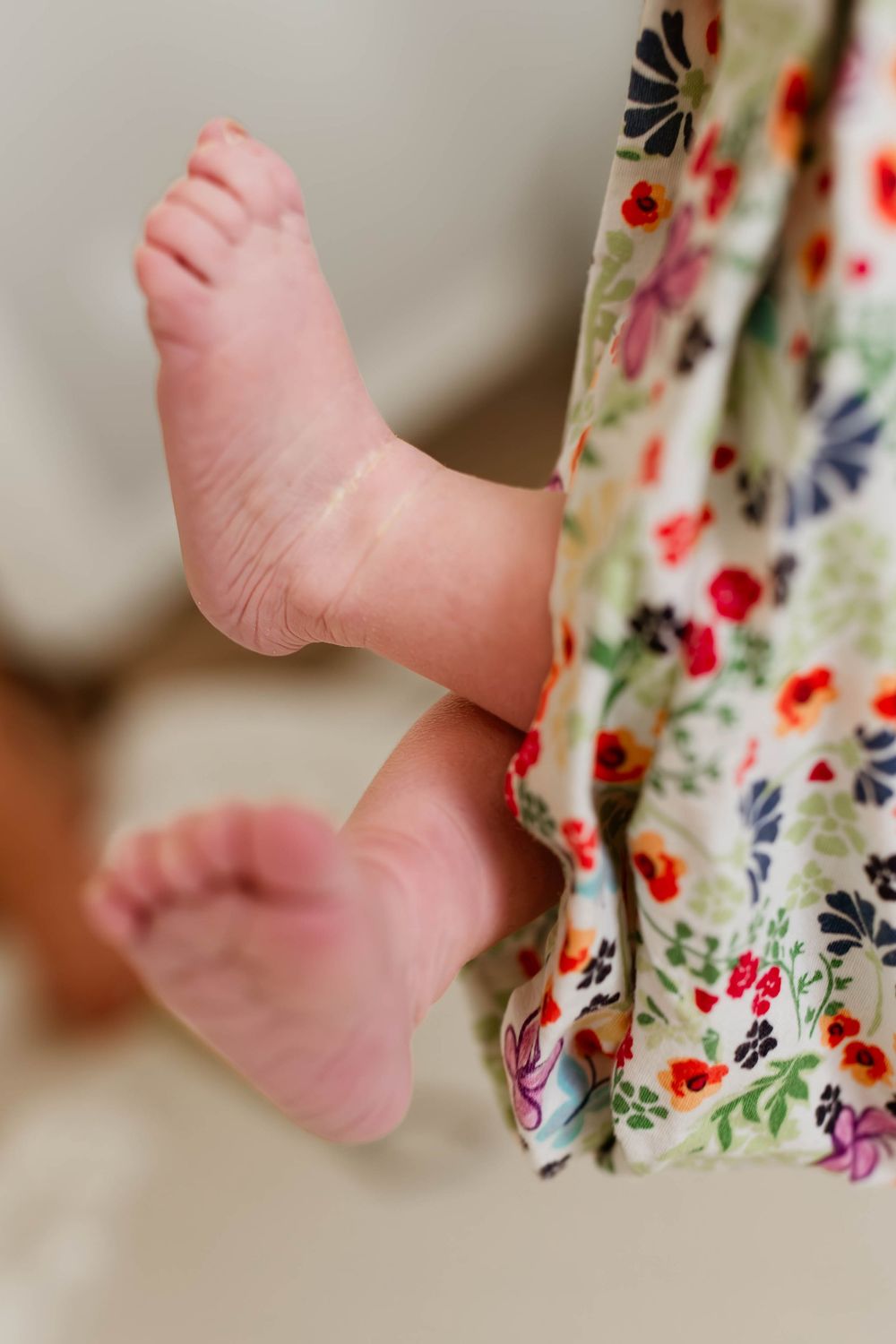 Close-up of tiny newborn baby feet peeking out from a colorful floral blanket.