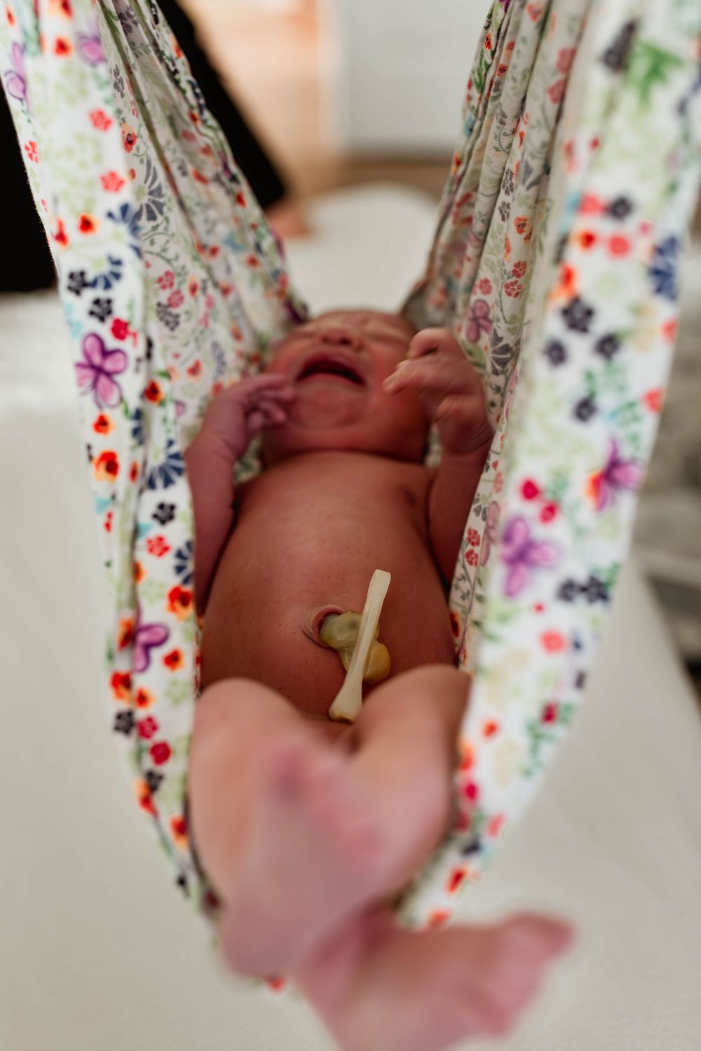 Newborn baby with umbilical cord clamp lying in a floral fabric sling during a home birth.