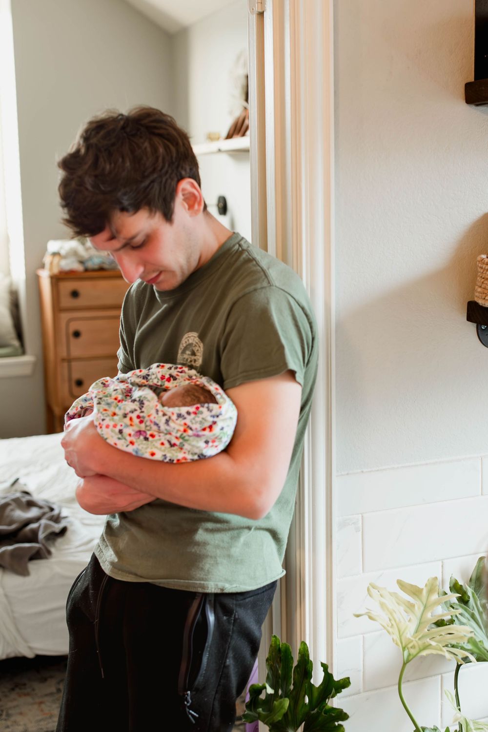 Young father in green shirt lovingly cradling his swaddled newborn baby at home.