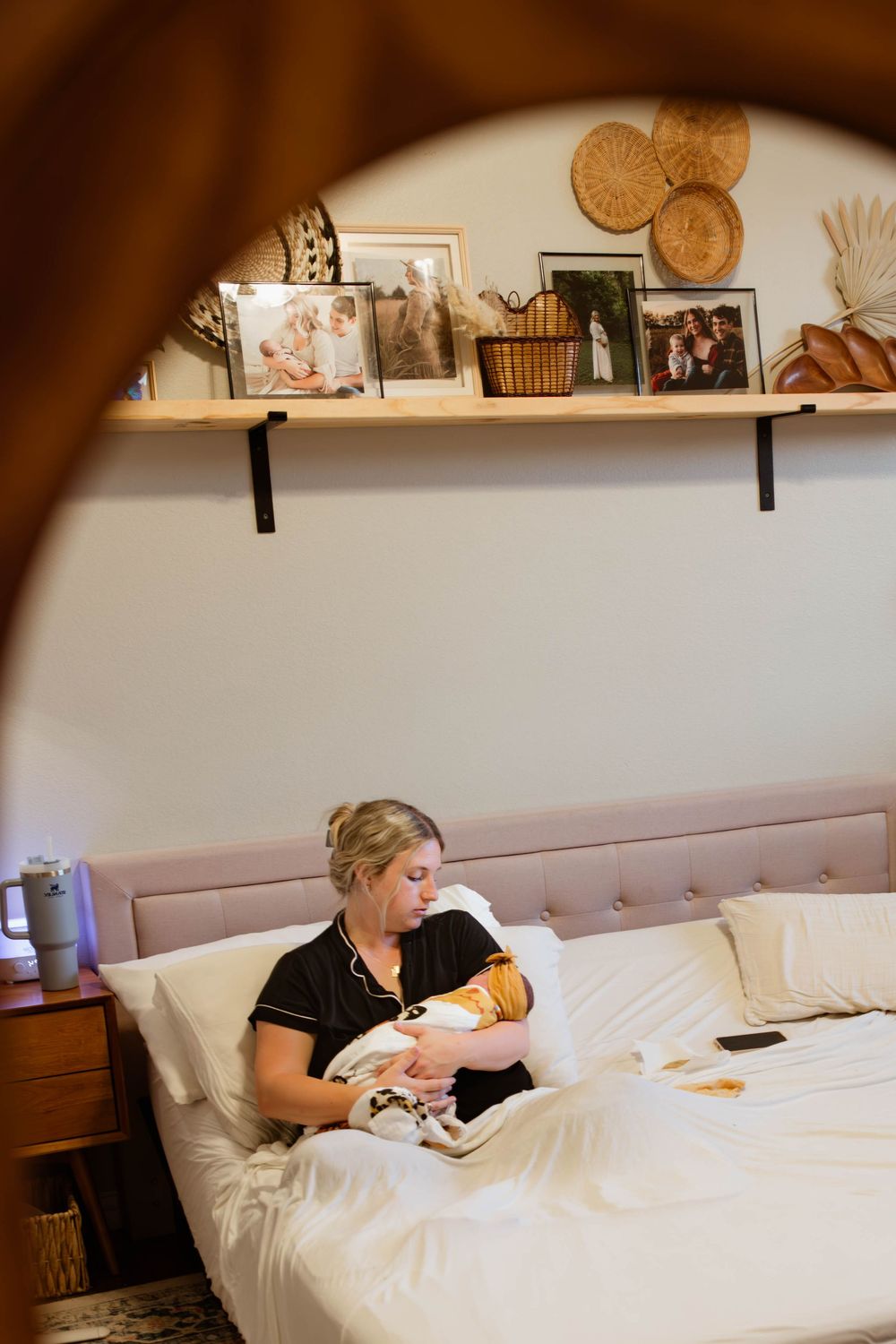 New mother breastfeeding newborn baby on a bed viewed through a decorative mirror arch.