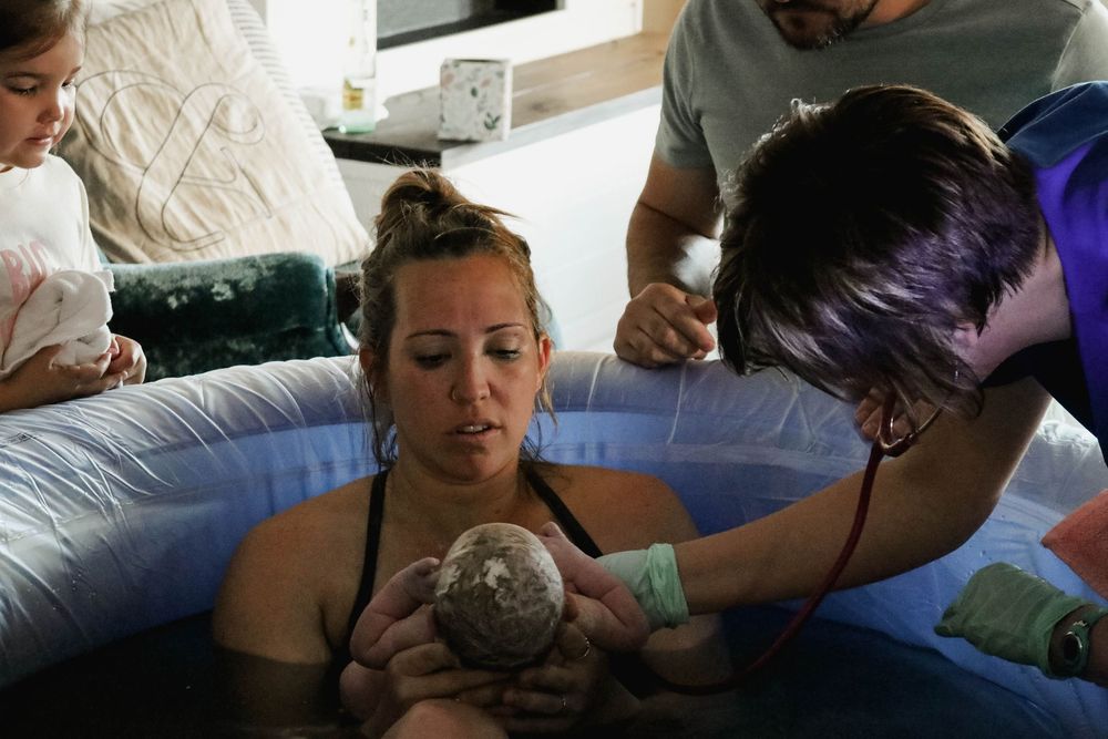Woman in labor holding newborn in an inflatable birth pool during a home water birth.