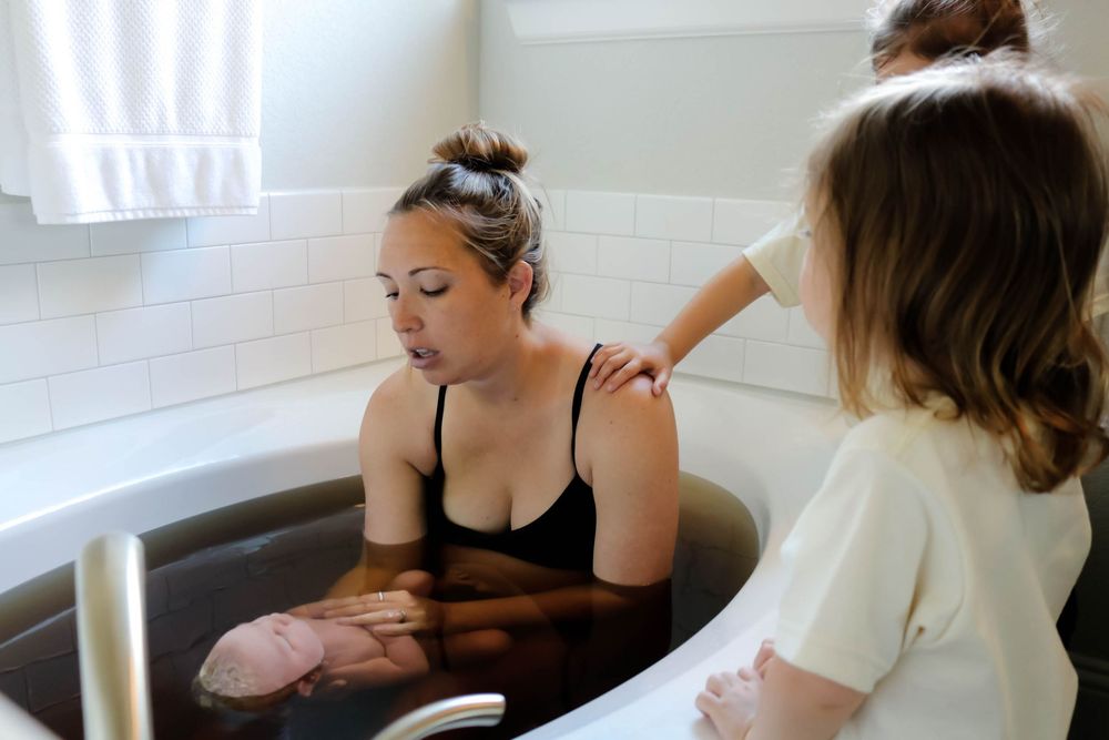 Woman laboring in a dark water birth tub with a midwife and support person assisting.