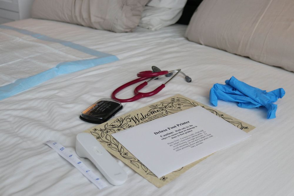 Home birth midwife supplies including stethoscope, gloves, and welcome card laid on a bed.