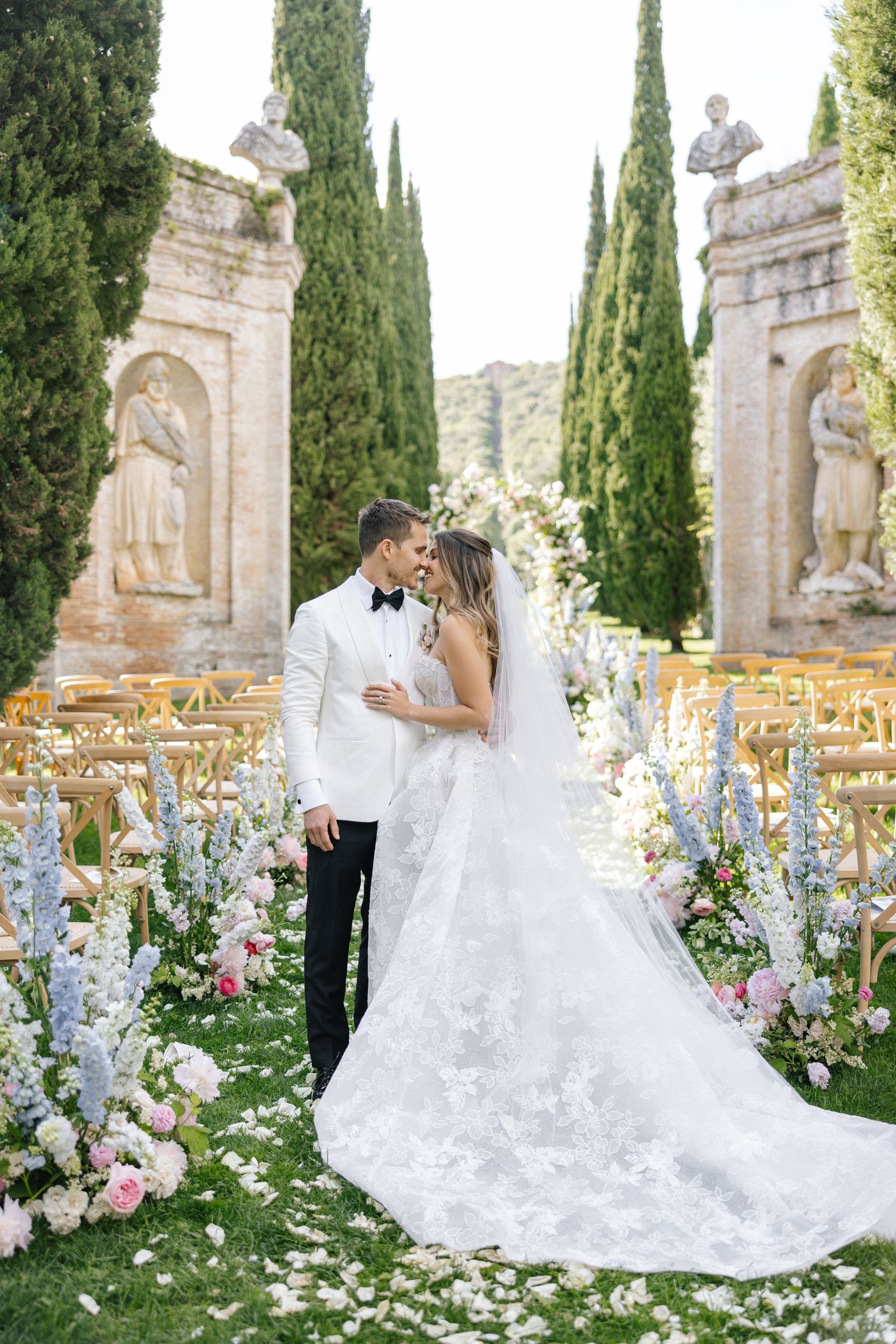 Bride in flowing white gown poses near fountain outside French chateau.