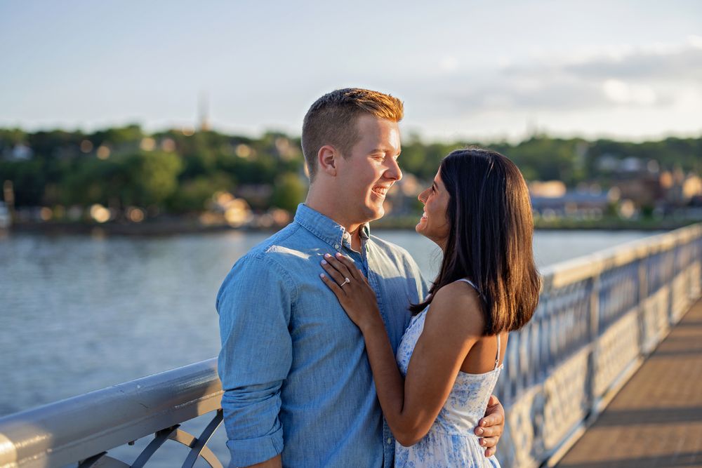 Couple gazing at each other tenderly on a waterfront bridge during golden hour sunset light.
