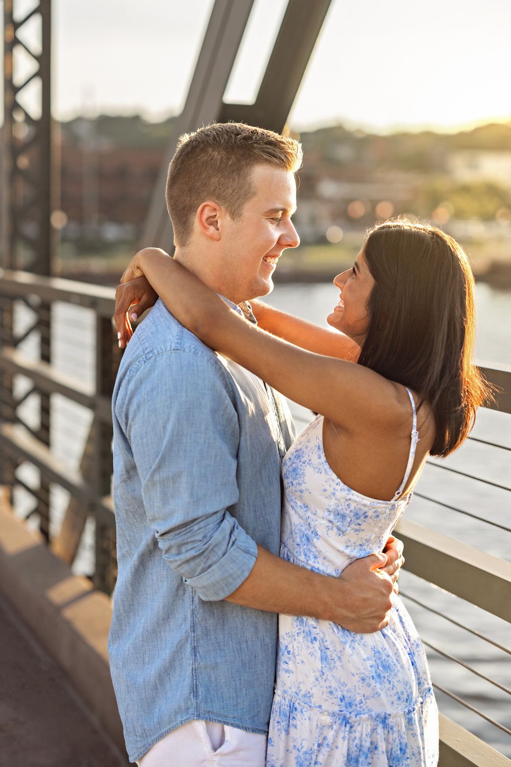 Couple embracing and smiling at each other on the Stillwater Bridge at golden hour.
