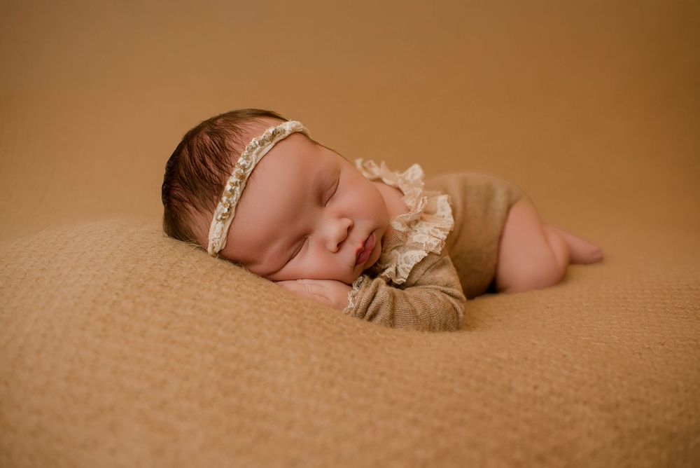Peaceful newborn sleeping on textured brown blanket in artistic photography setup.