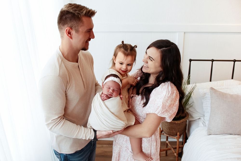 Intimate family portrait session in a bright white bedroom with modern decor.