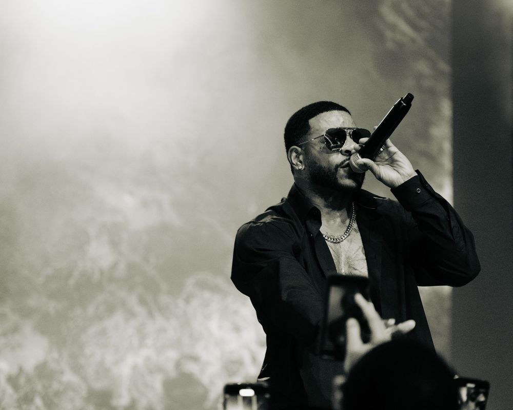 A male singer in a black jacket performs with a microphone in a black and white concert photo.