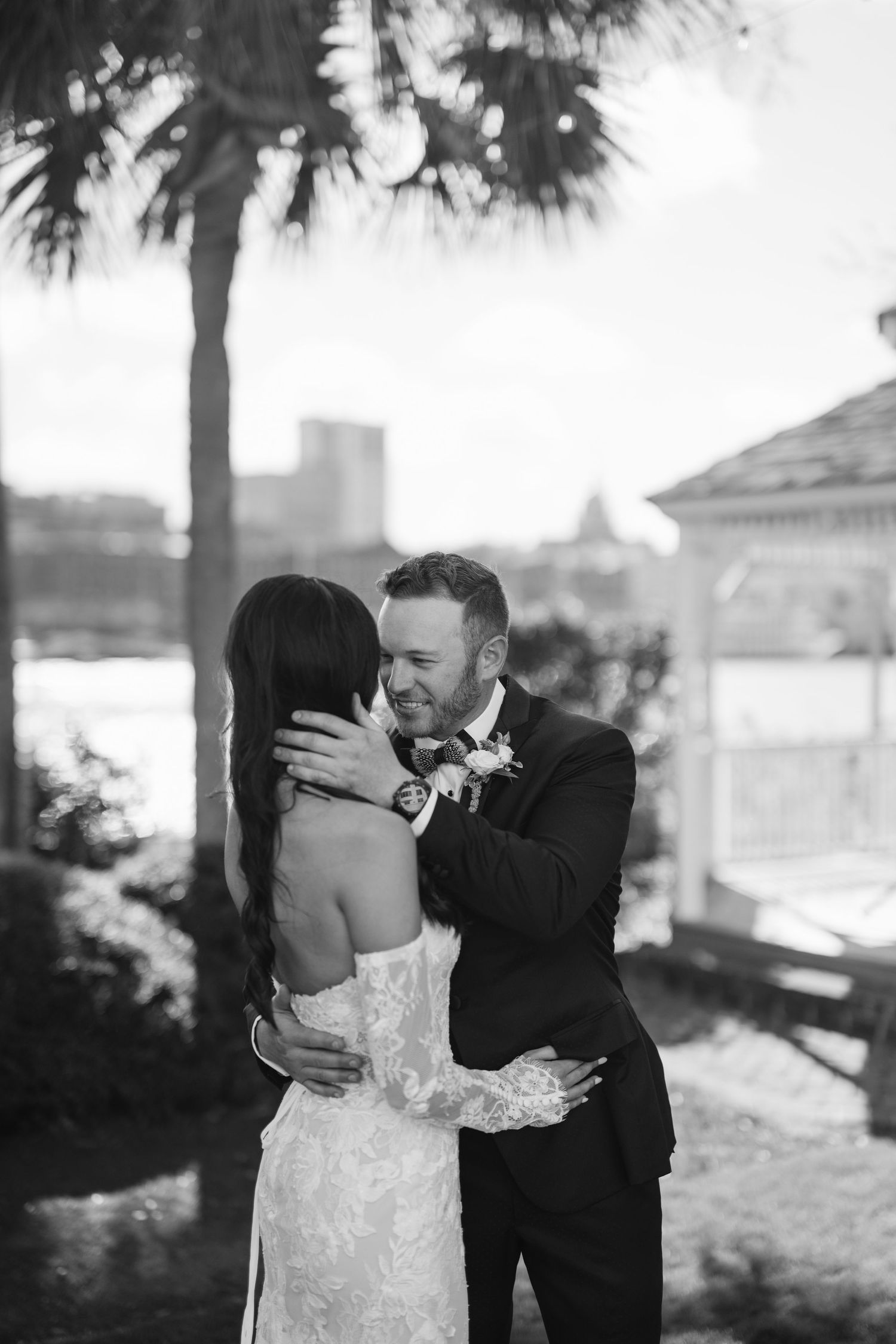 Bride and groom share an emotional first look embrace outdoors near a gazebo and palm trees on their wedding day.