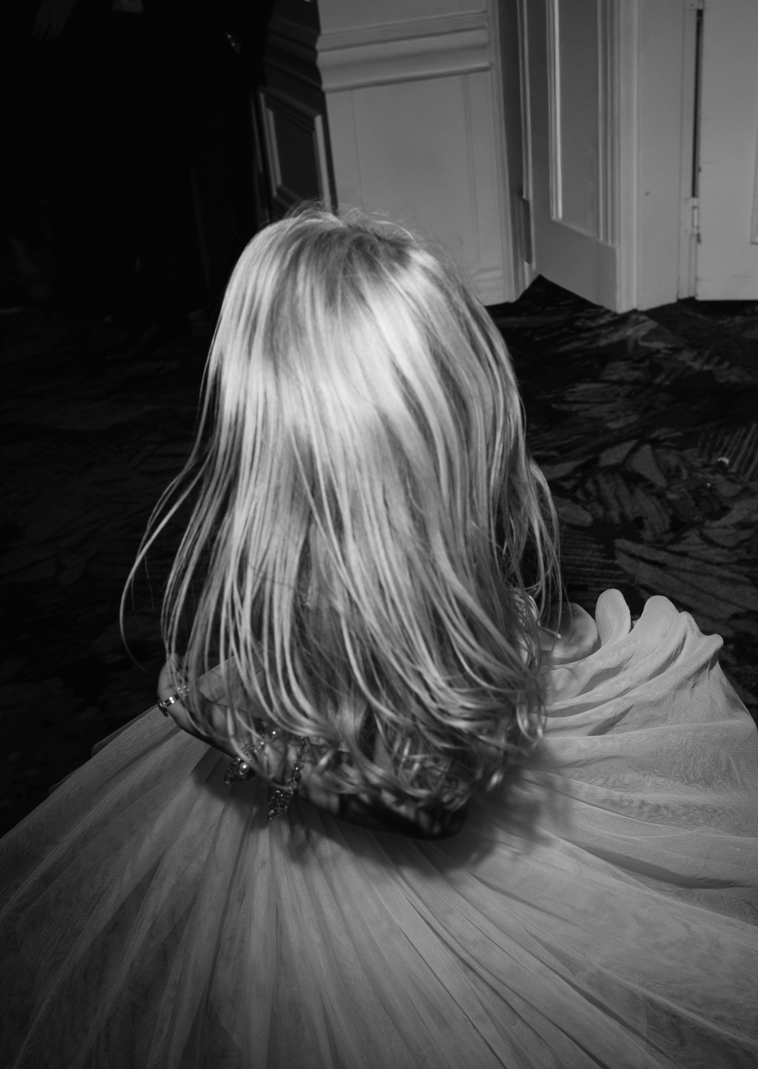 Black and white photo of flower girl with long blonde hair wearing a tulle dress at a wedding reception.
