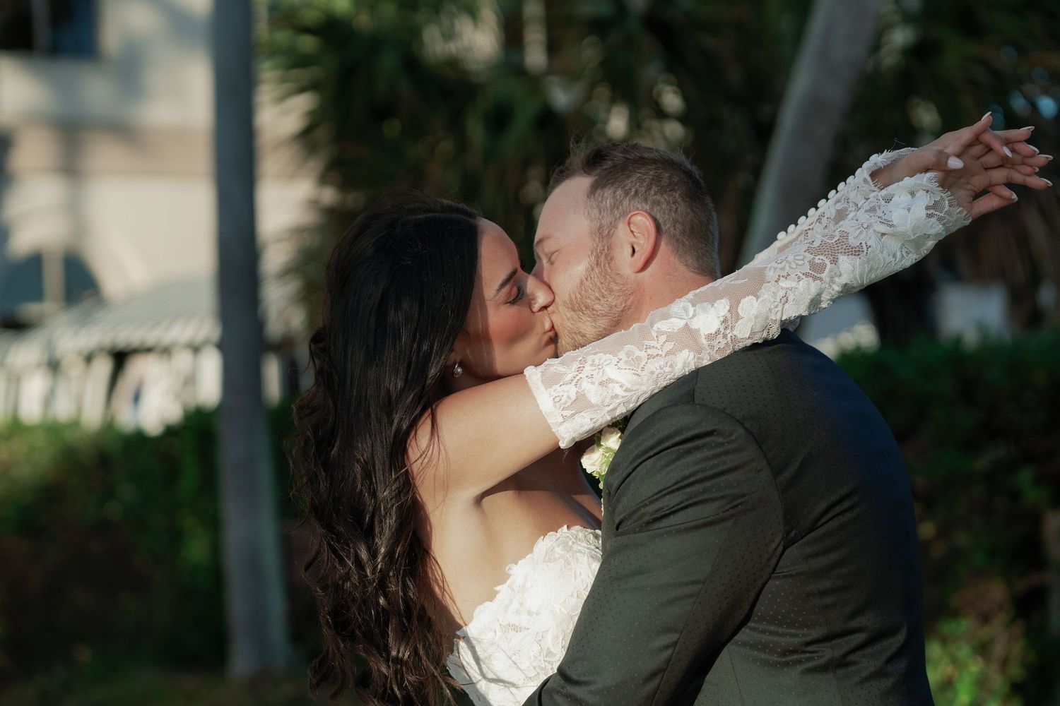 Bride and groom sharing romantic first kiss outdoors after wedding ceremony surrounded by greenery.