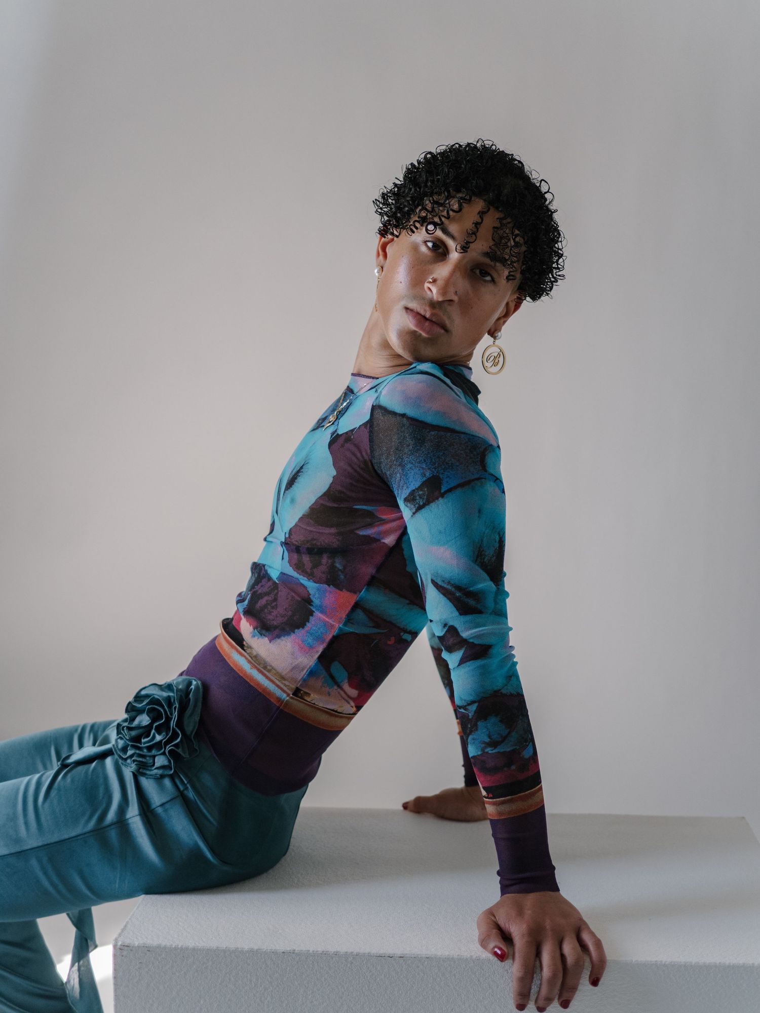 Model poses in colorful teal abstract print long-sleeve top with purple pants and gold hoop earring.