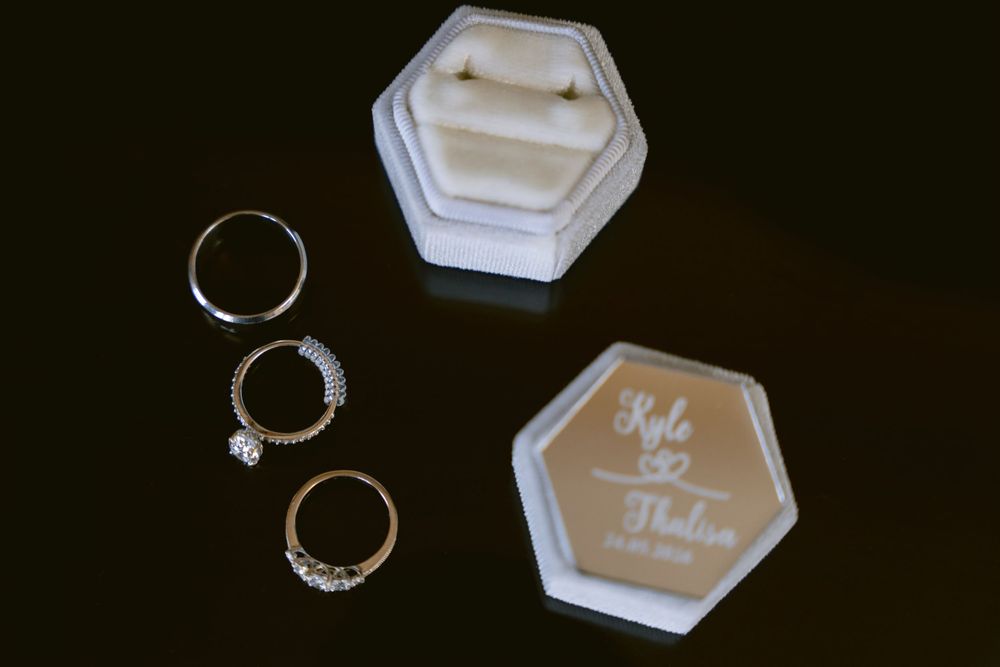 Three wedding rings beside personalized hexagonal ring boxes engraved with Kyle and Madison on a dark surface.