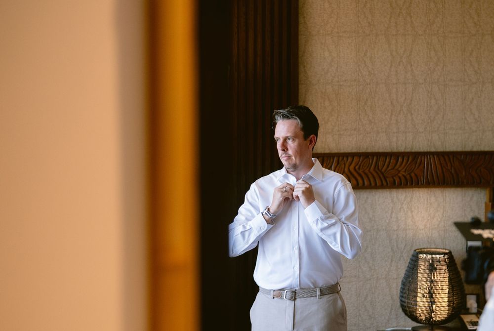 Groom in white dress shirt adjusting his collar while getting ready for his wedding ceremony.