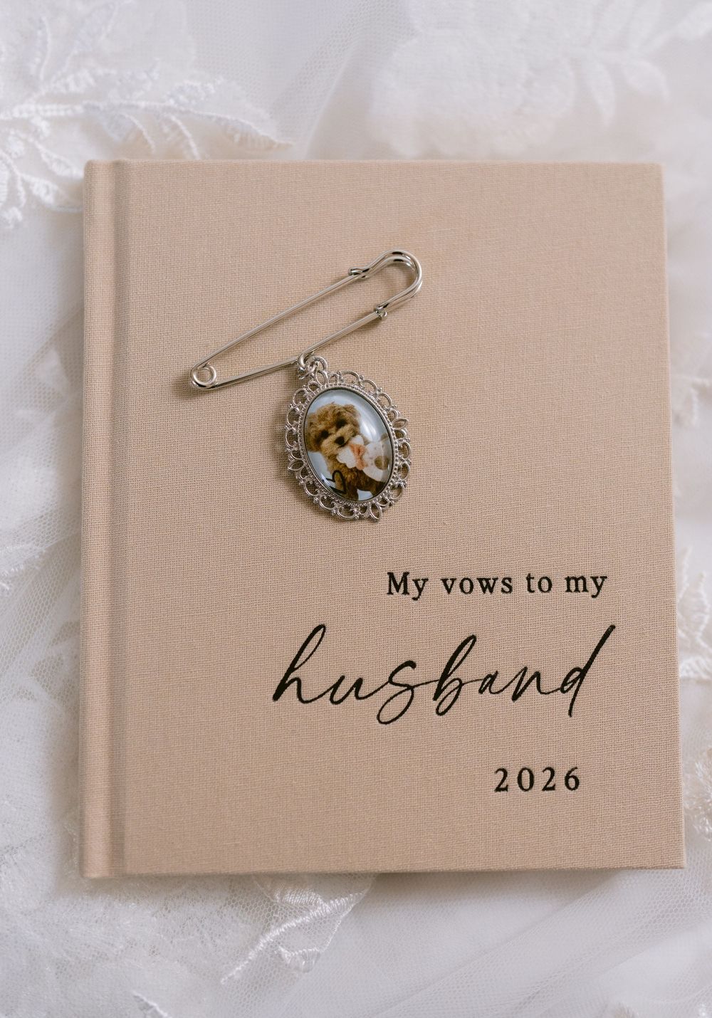 Beige hardcover vow book reading My Vows to My Husband 2026 with a vintage oval photo brooch pin on top.