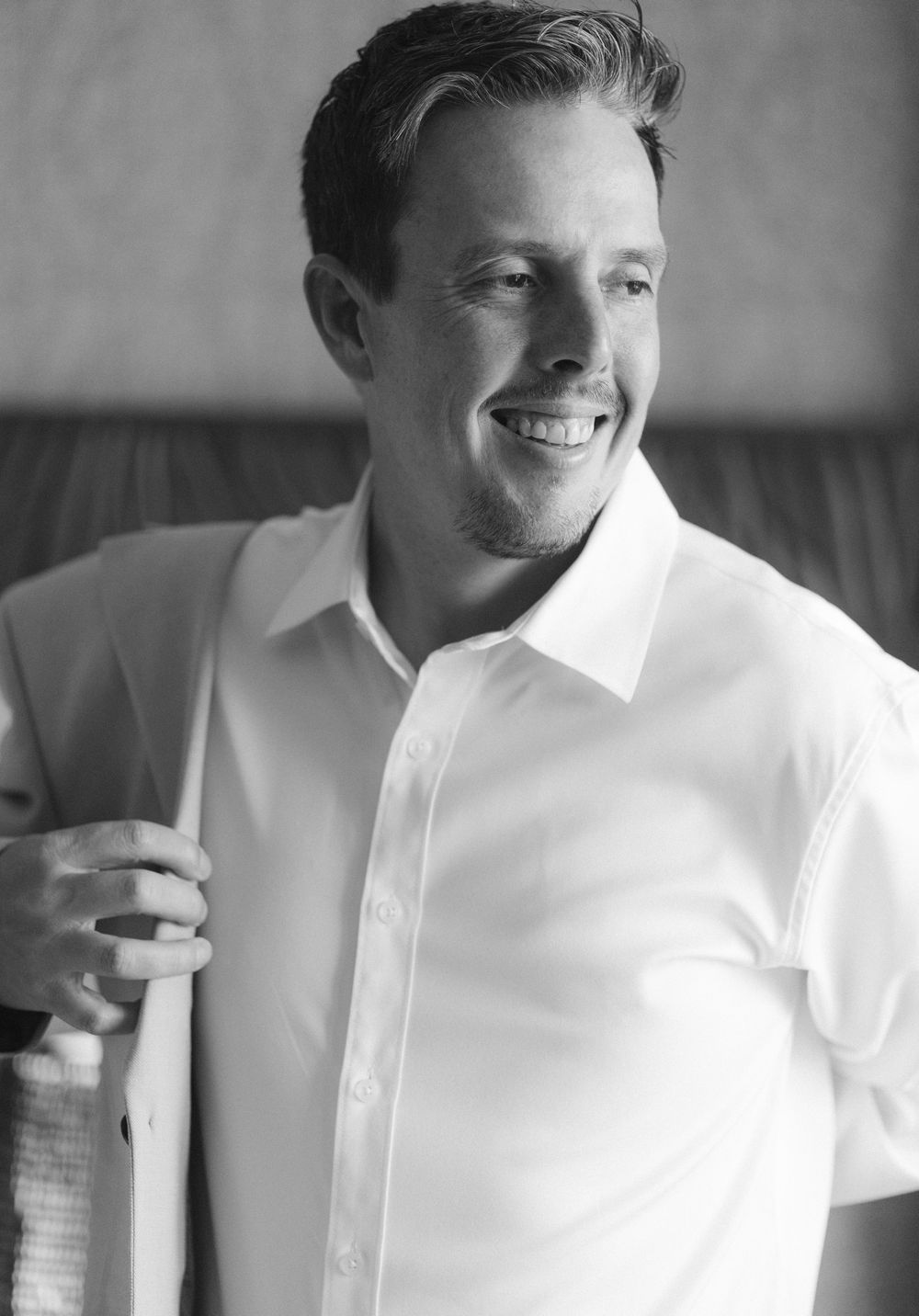 Smiling man in white dress shirt putting on suit jacket, black and white portrait photo.