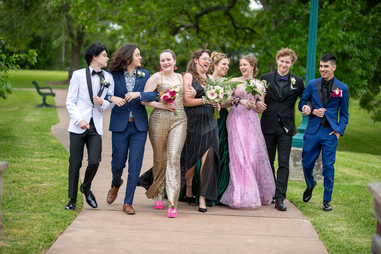 Wedding party walking and laughing together on a green lawn path.