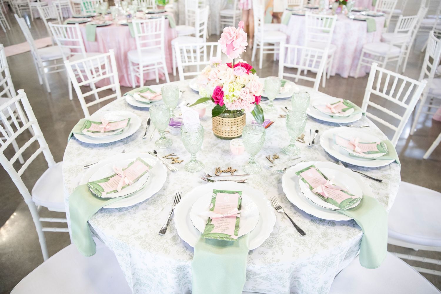 Wedding reception tables set with elegant white and pink place settings and floral centerpieces.