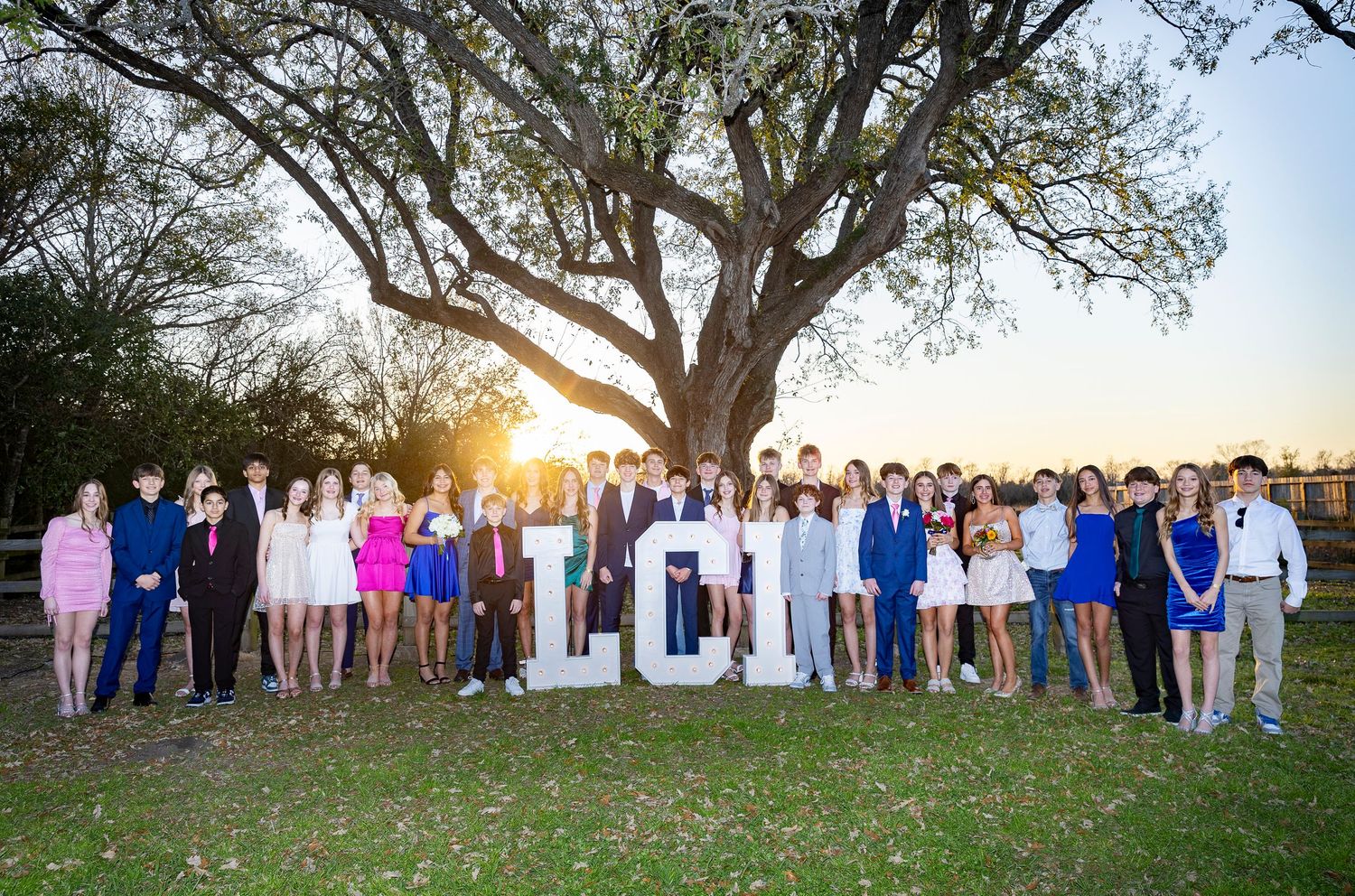 Large group photo taken at sunset under a sprawling oak tree.