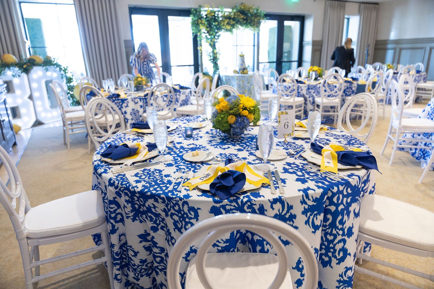 A formal dining room setup with blue and white floral tablecloths and elegant place settings in a bright space.