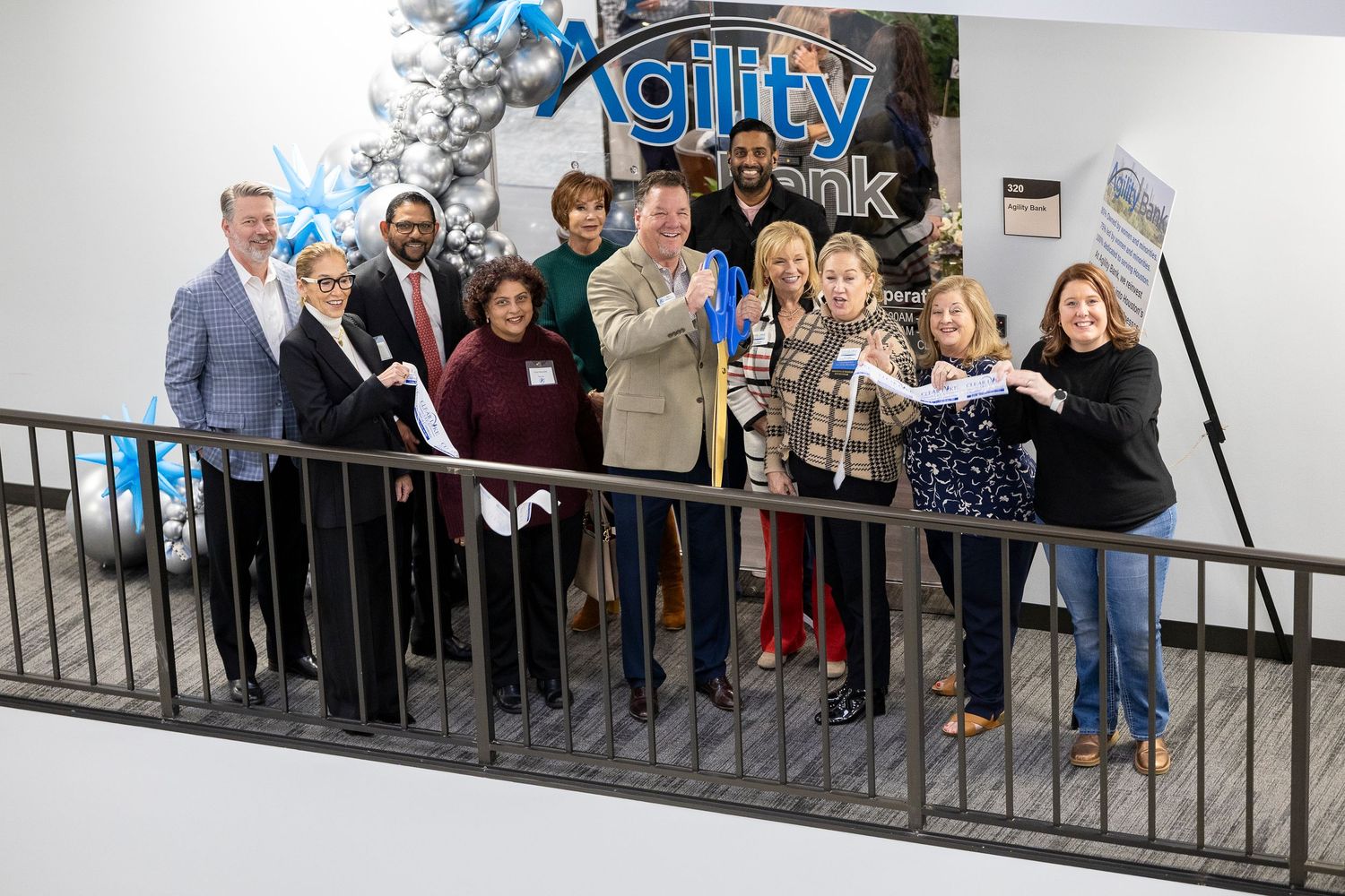 Group of professionals celebrate a ribbon cutting ceremony at Agility office with festive holiday decorations.