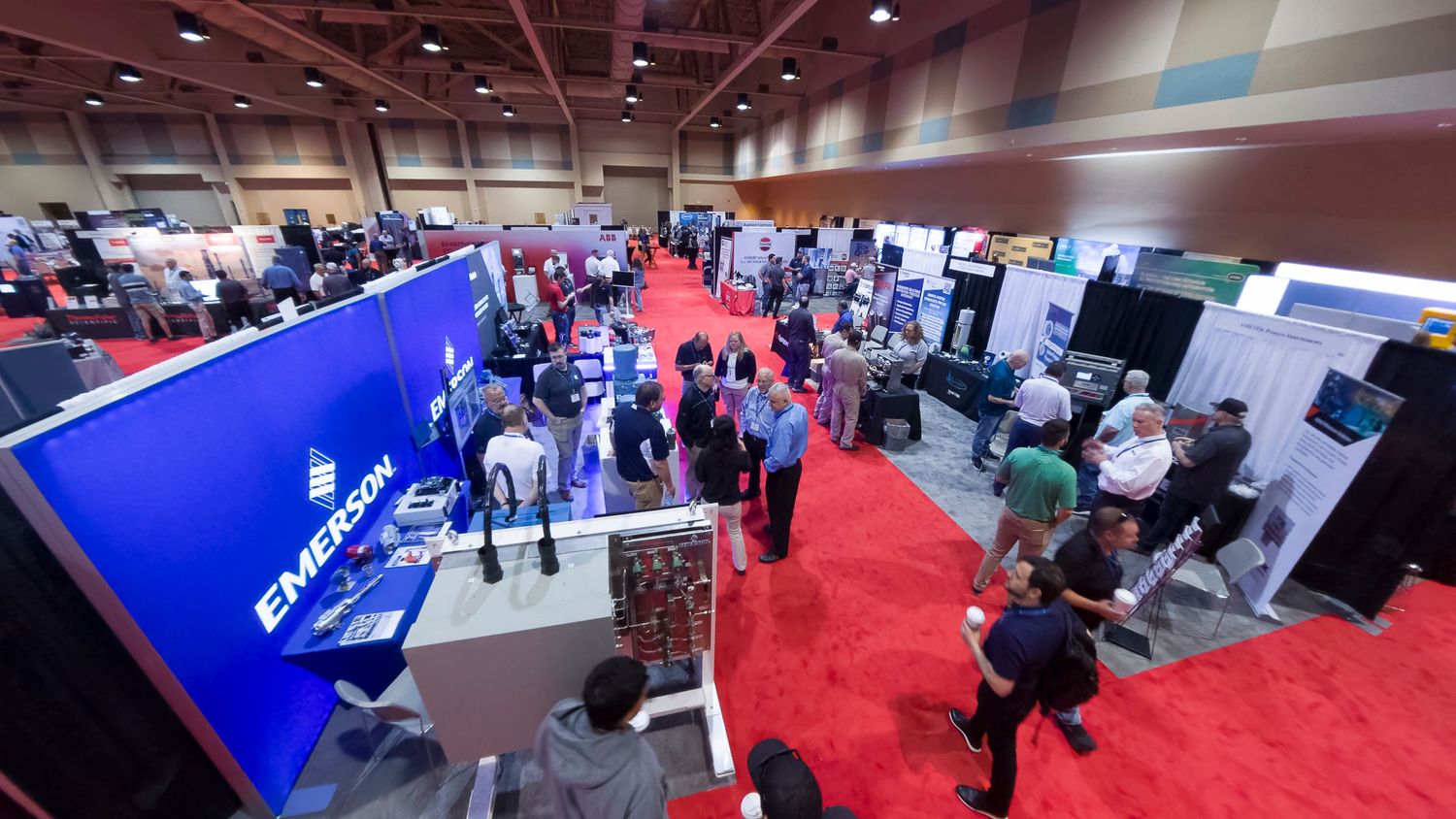 Aerial view of a busy trade show floor with Emerson booth and attendees networking among colorful exhibits.