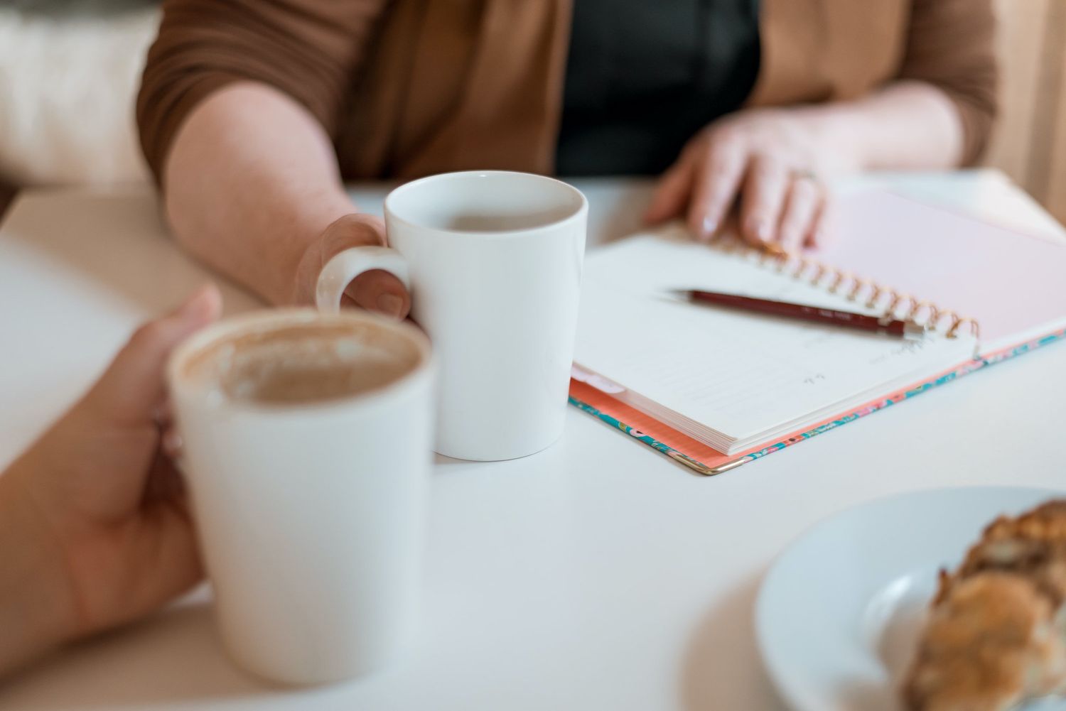 Two coffee cups and a notebook on a white table during a meeting.