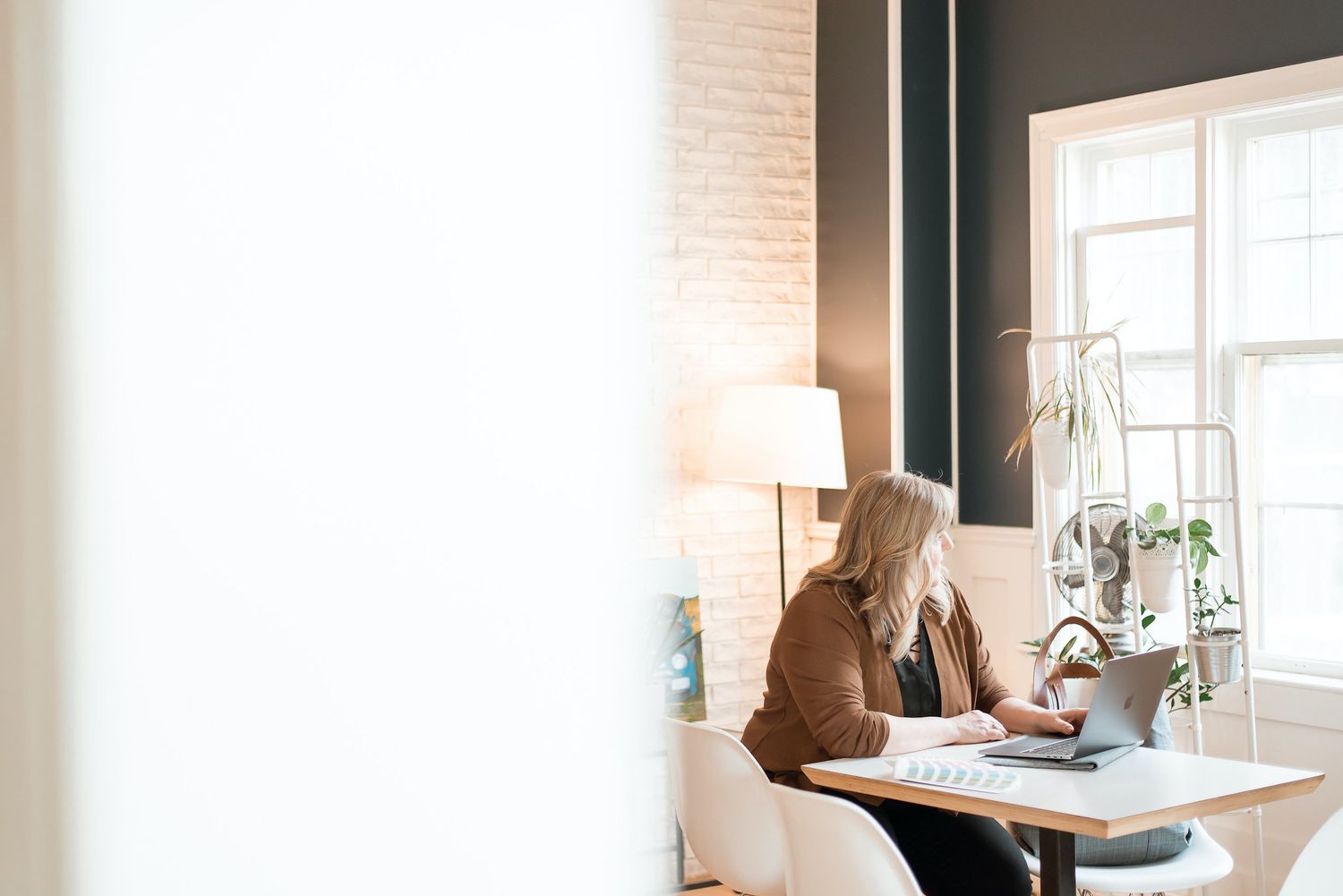 Bright modern workspace with white brick wall and window featuring contemporary office furniture.
