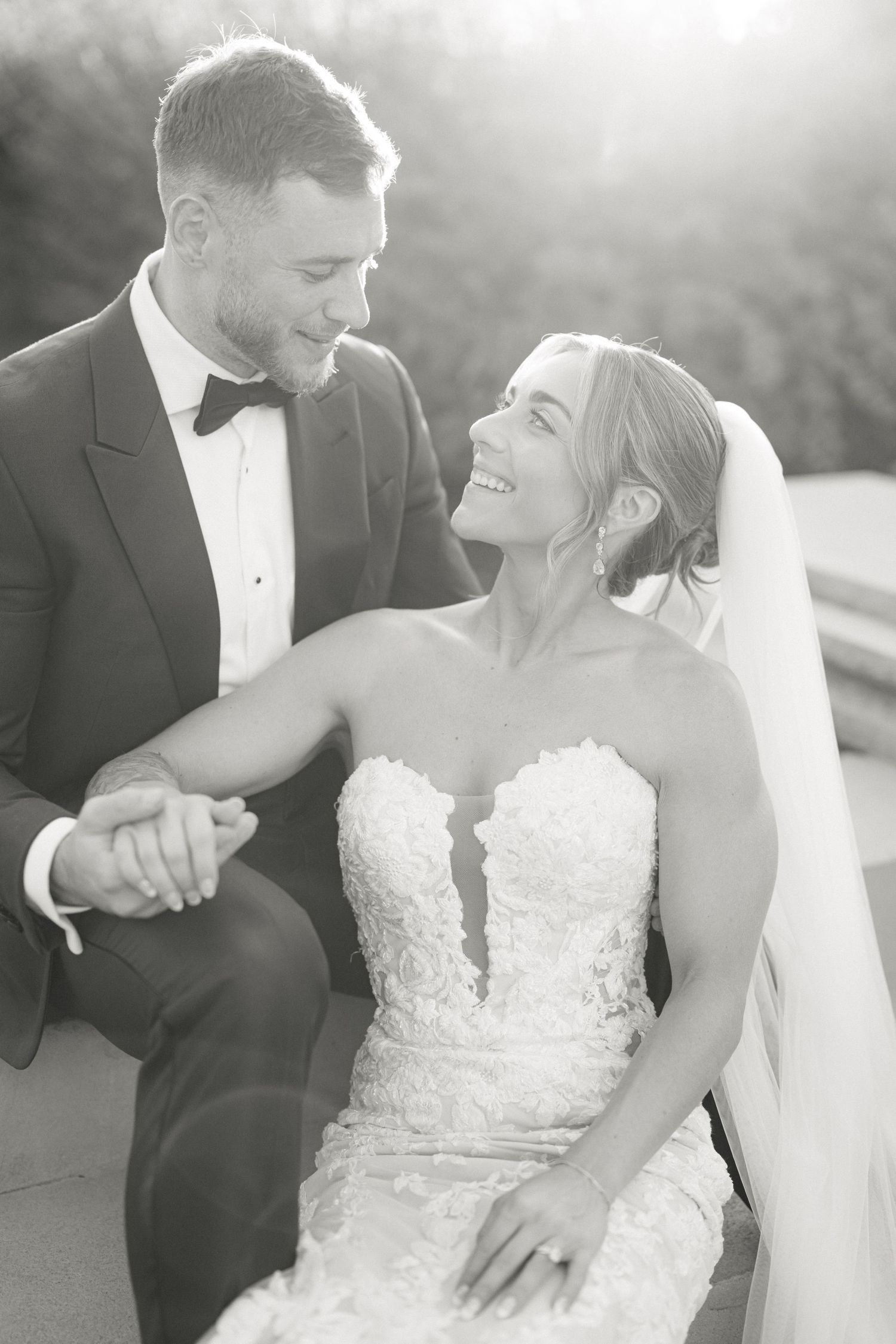 Armour House Wedding - Black and white wedding photo of a smiling bride in lace gown and groom in tuxedo holding hands outdoors.