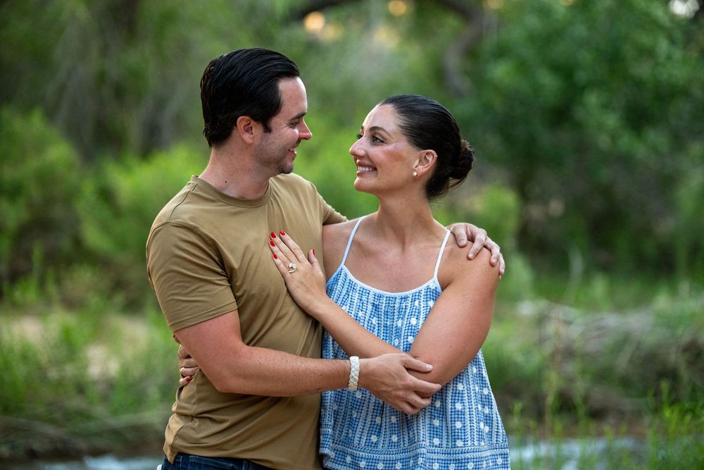 Couple embracing and smiling at each other outdoors in a lush green park setting.