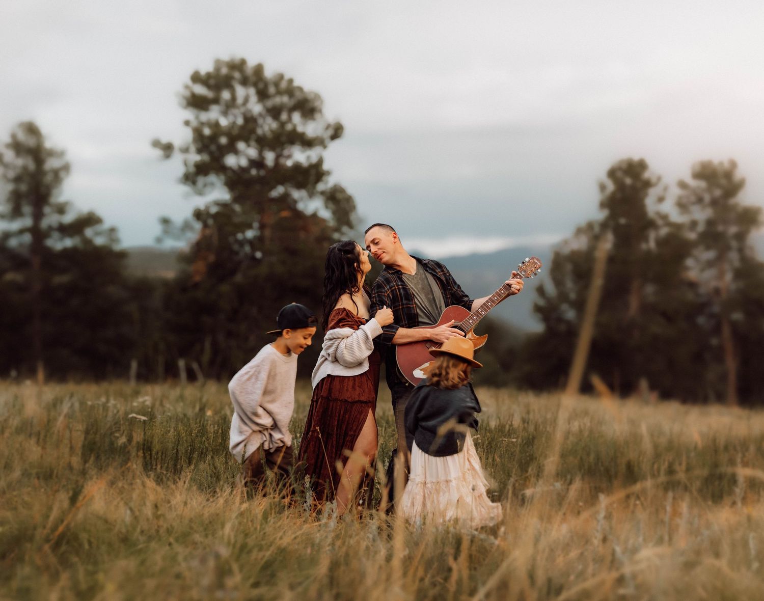 A family enjoying a playful moment in a rustic field with mountains in the background.