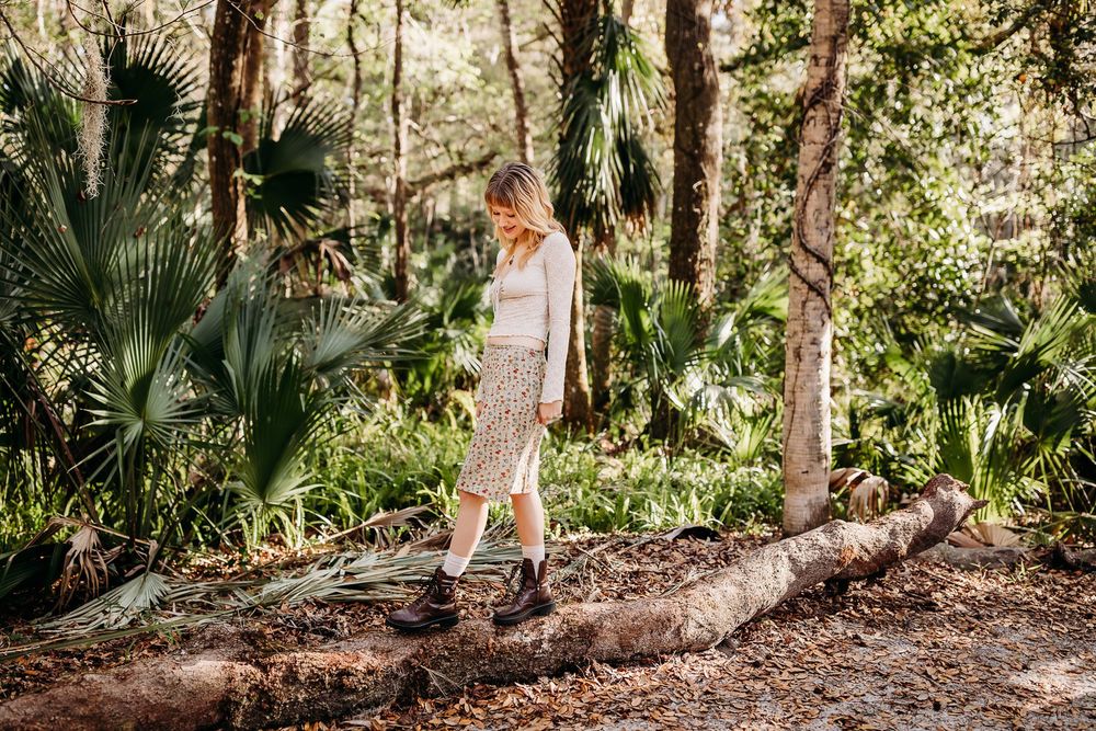 A person walking on a fallen log in a lush tropical forest surrounded by palm fronds and dappled sunlight.